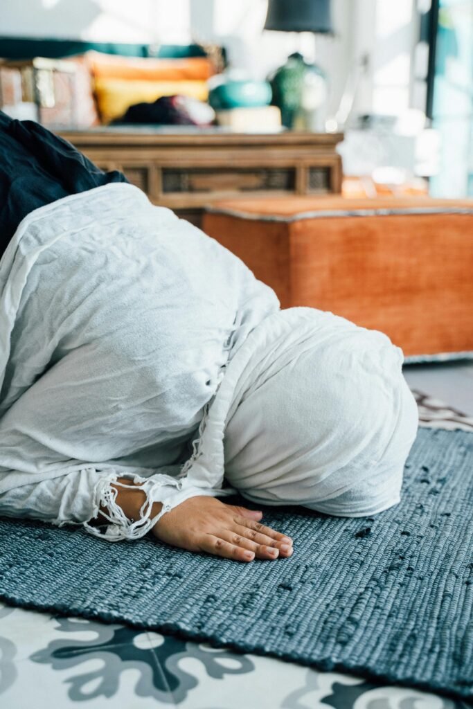 Woman in headscarf praying on a rug inside a room with vibrant decor.